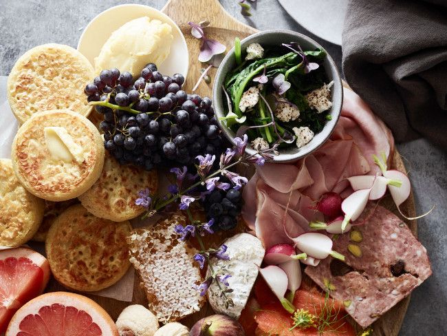 Homemade crumpets on a stunning breakfast board with fresh fruit, honey butter, and cured meats. 